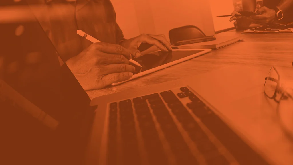 Pessoas trabalhando com notebook e tablet em mesa de reunião, em tratamento duotone laranja
